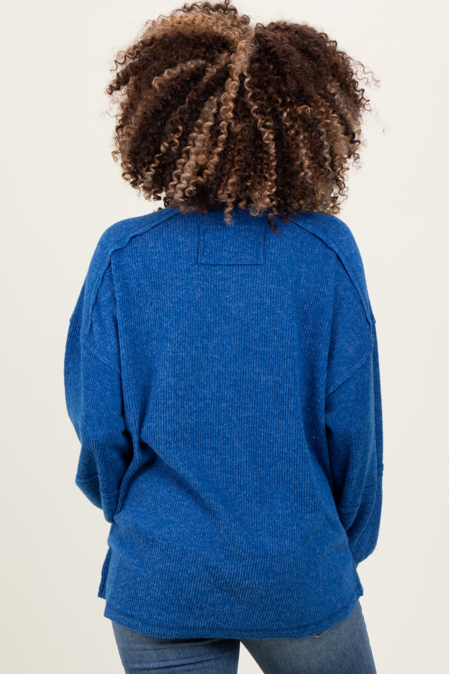 woman wearing a blue oversized maternity sweater, seen from the back, with a relaxed fit and ribbed texture