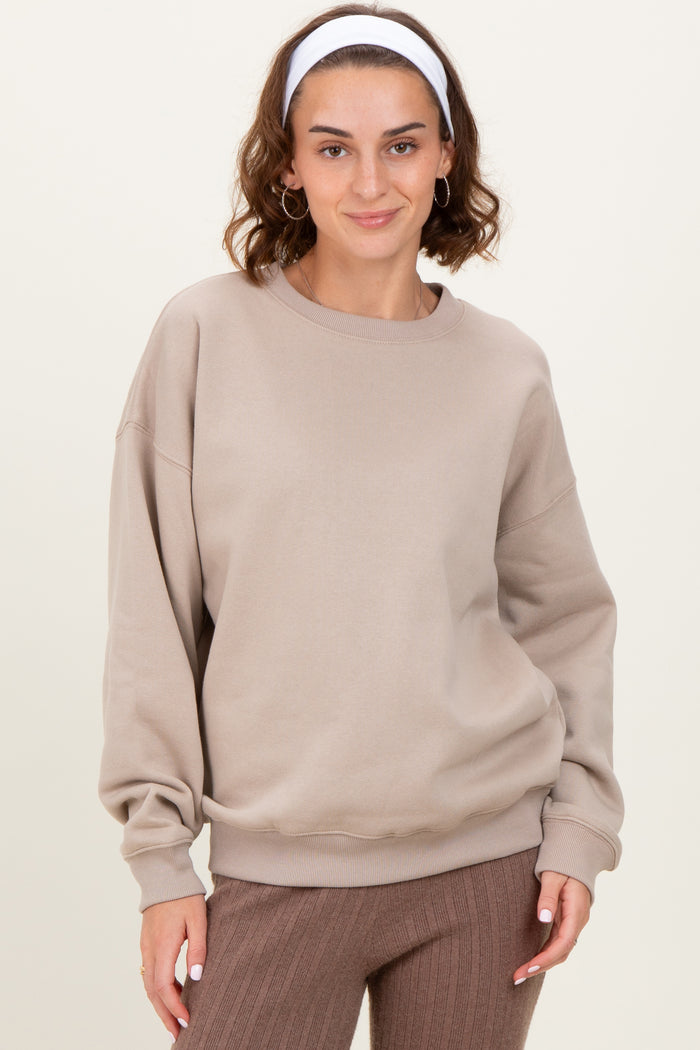 woman wearing a beige oversized sweatshirt with dropped shoulders and a round neckline, paired with brown ribbed pants