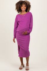 woman wearing a bright purple maternity sweater and matching skirt, holding her baby bump with a smile