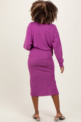 woman wearing a purple maternity sweater dress with a fitted skirt and long sleeves, showing her pregnancy silhouette from the back