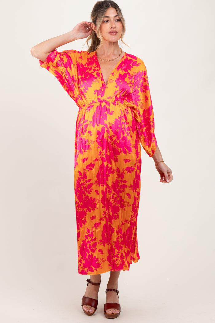 woman wearing a vibrant yellow and pink floral maternity dress with a deep v-neck and flowing sleeves, styled with brown heels