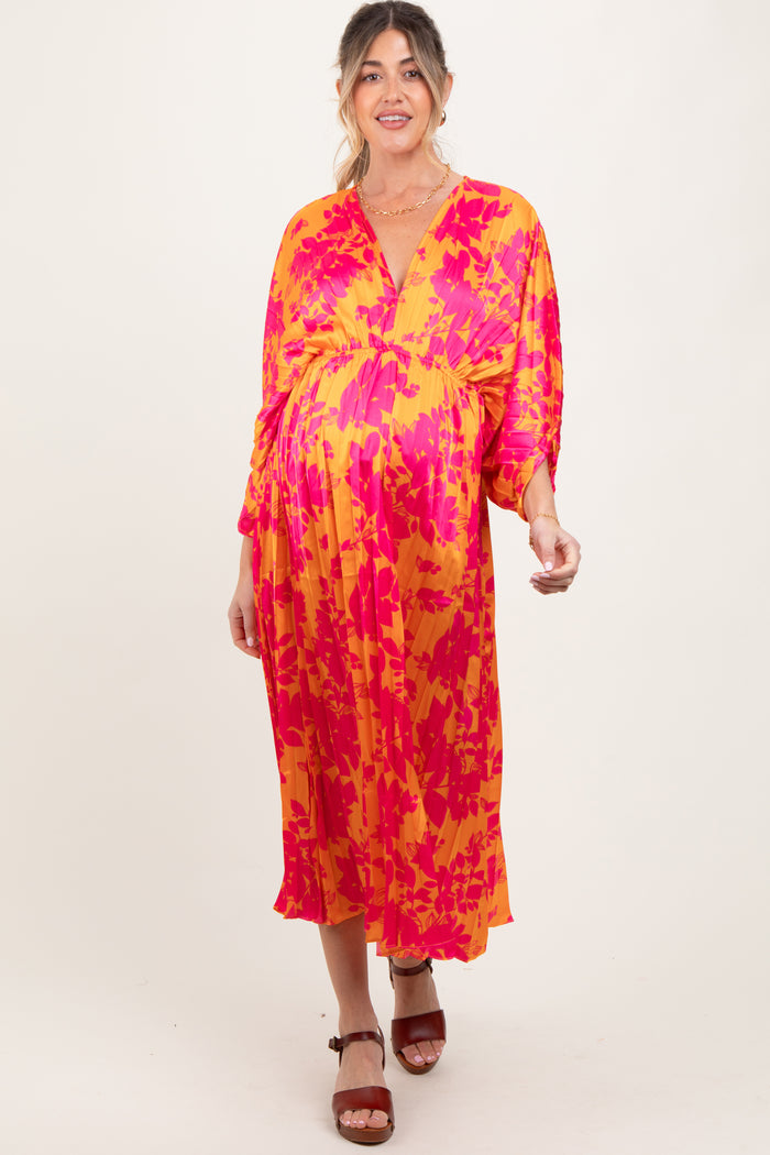 woman wearing a vibrant pink and orange patterned maternity dress with a v-neckline and three-quarter sleeves, displaying a baby bump