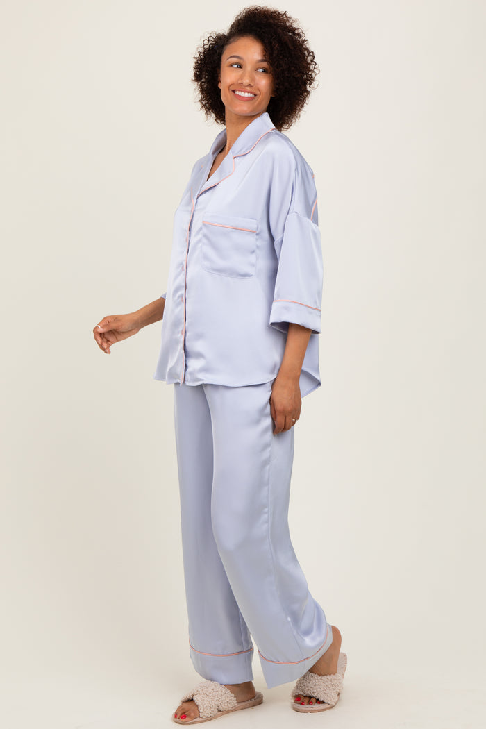 woman wearing a light blue satin pajama set with short sleeves and piping details, styled with soft slippers