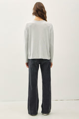 woman wearing a light gray long sleeve top and black wide-leg jeans, viewed from the back