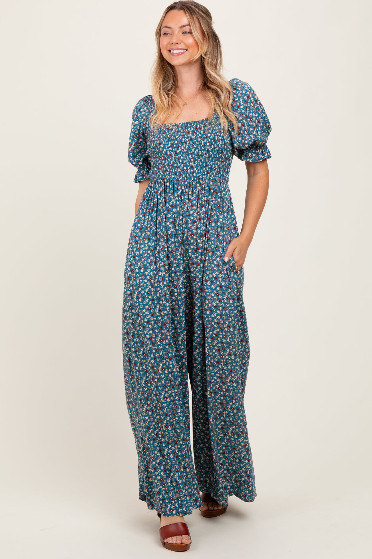 woman wearing a blue floral maxi dress with puff sleeves and pockets, smiling against a neutral background