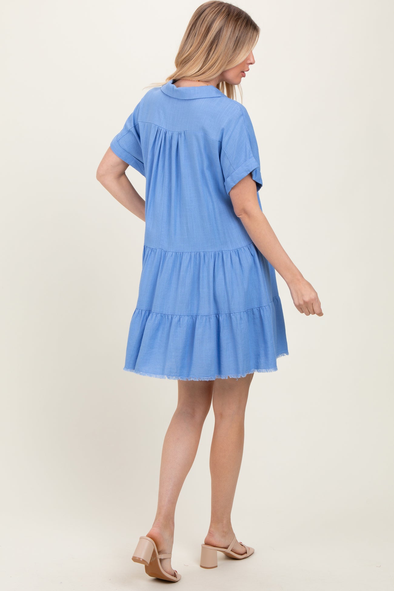 woman wearing a blue tiered short sleeve dress with a frayed hem and sandals, standing with her back to the camera