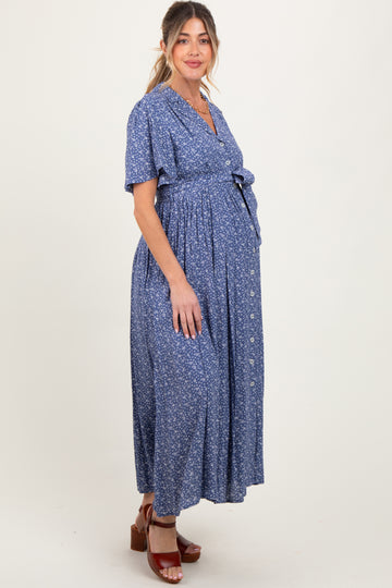 woman wearing a blue floral maternity maxi dress with a tie waist and buttons, showcasing her baby bump