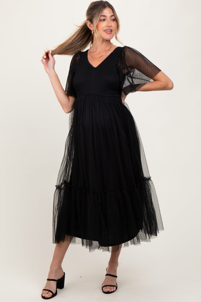 woman wearing a black maternity dress with puff sleeves and tulle detailing, showing her baby bump