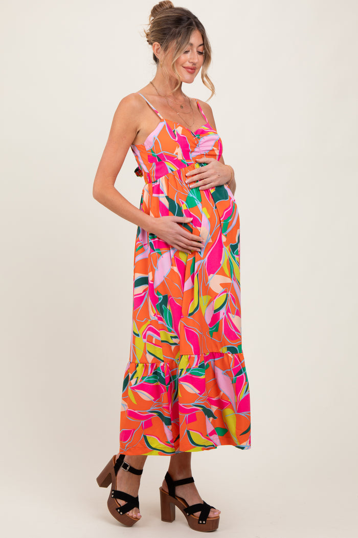 woman wearing a vibrant pink floral maternity dress with a ruffled hem and holding her baby bump