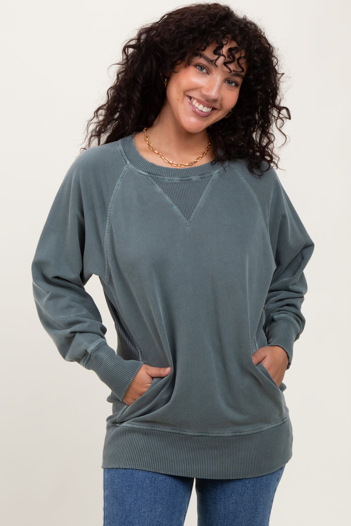 woman wearing a green oversized sweatshirt with a v-neck and side pockets, smiling at the camera