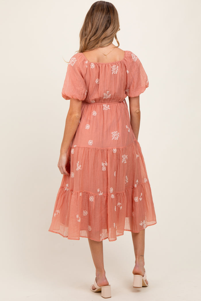 woman wearing a coral maternity dress with floral embroidery and tiered skirt, showing off her baby bump from the back