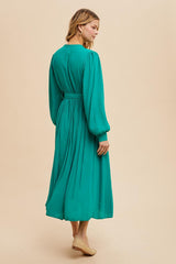 woman wearing a teal long sleeve maxi dress with a cinched waist and flowing skirt, viewed from the back