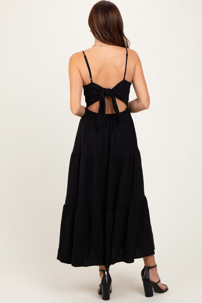 woman wearing a black tiered maxi dress with a bow tie back detail and spaghetti straps