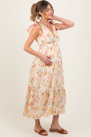 woman wearing a floral maternity dress with pink bow straps, holding her baby bump and smiling
