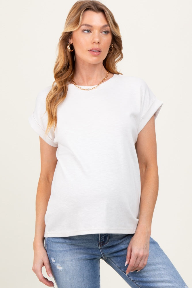 woman wearing a light beige short sleeve maternity top with rolled cuffs and a relaxed fit, showing her baby bump