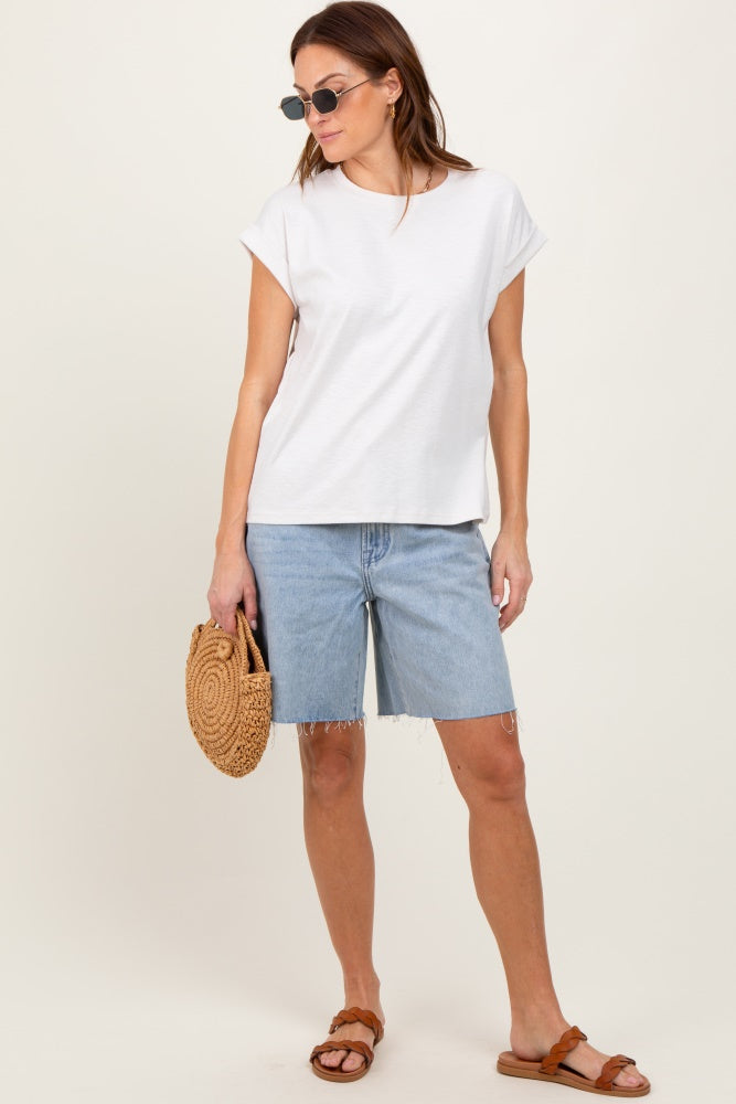 woman wearing a white short sleeve top and light blue denim shorts, holding a straw bag and wearing sunglasses