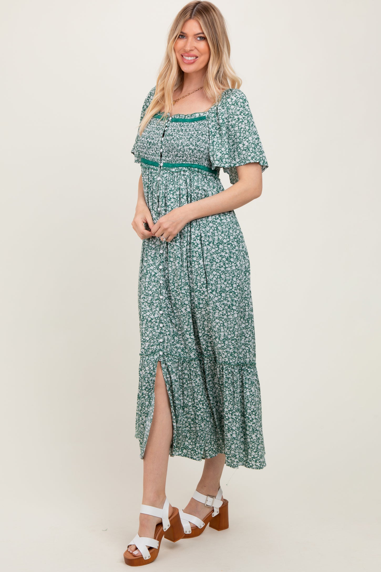 woman wearing a green floral maxi dress with short sleeves and a side slit, standing and smiling