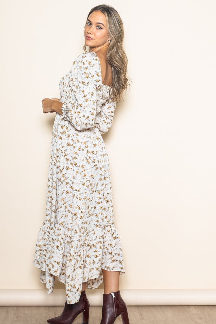 woman wearing a white floral midi dress with puff sleeves and a ruffled hem, posing sideways against a plain background