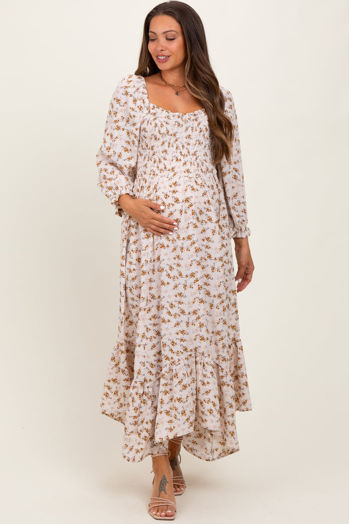 woman wearing a floral print maternity maxi dress with a smocked bodice and tiered hem, gently cradling her baby bump
