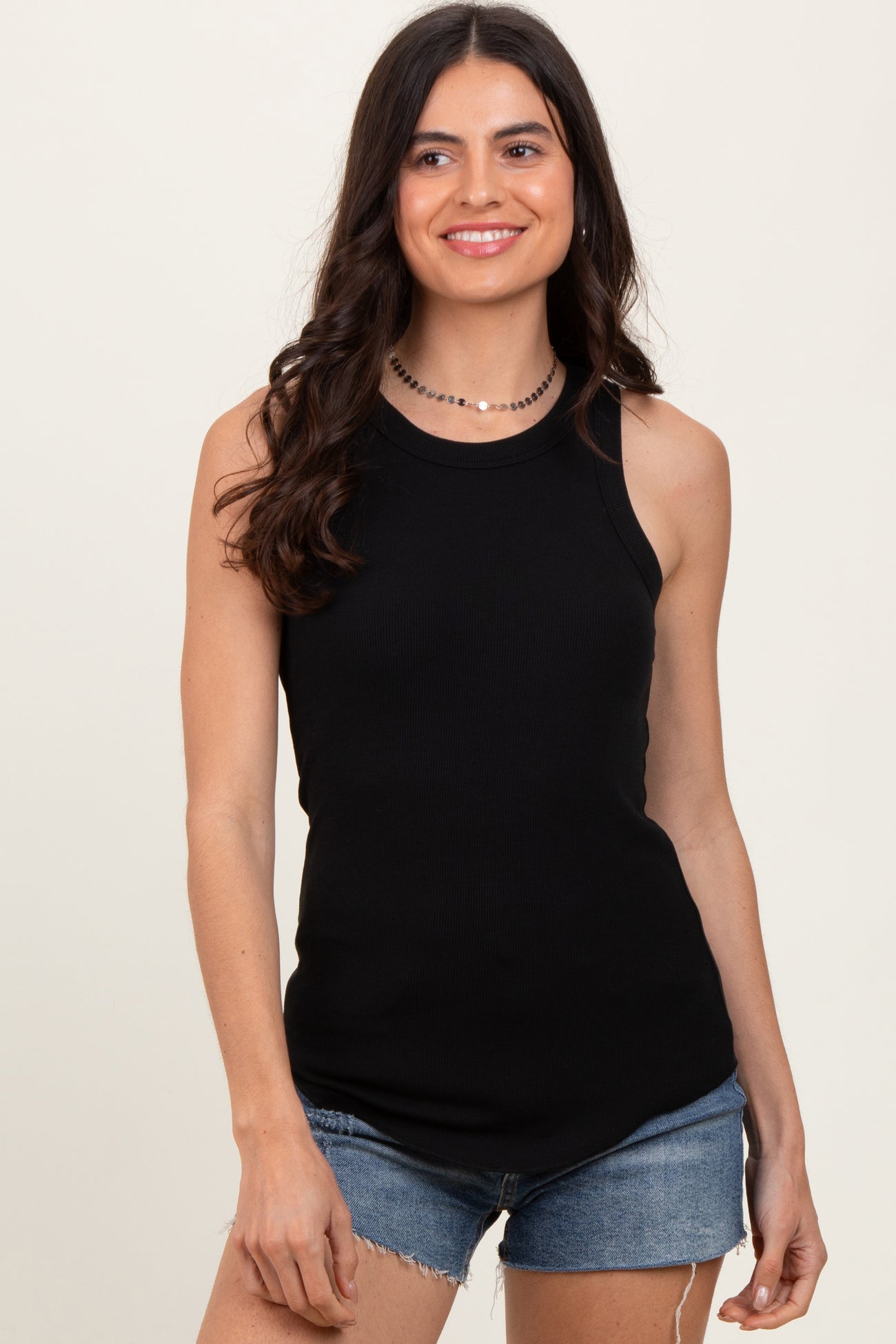 woman wearing a black ribbed tank top and denim shorts, smiling at the camera