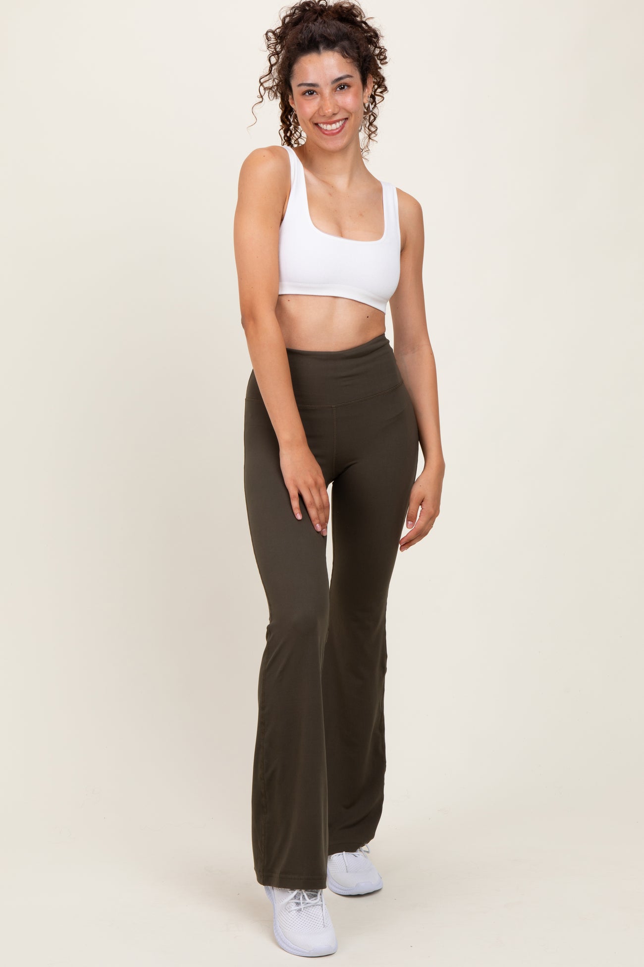 woman wearing a white cropped tank top and olive green flared leggings