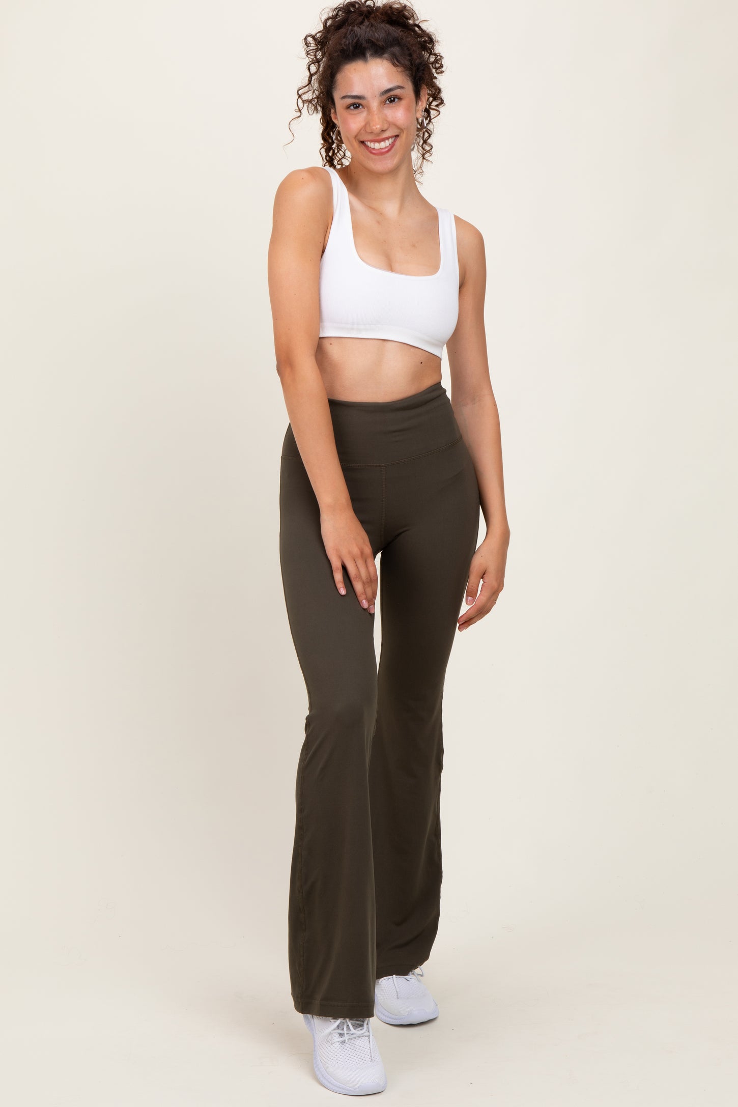 woman wearing a white cropped tank top and olive green flared leggings