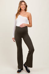 woman wearing a white one-shoulder top and olive green maternity flared leggings, smiling, with a baby bump visible