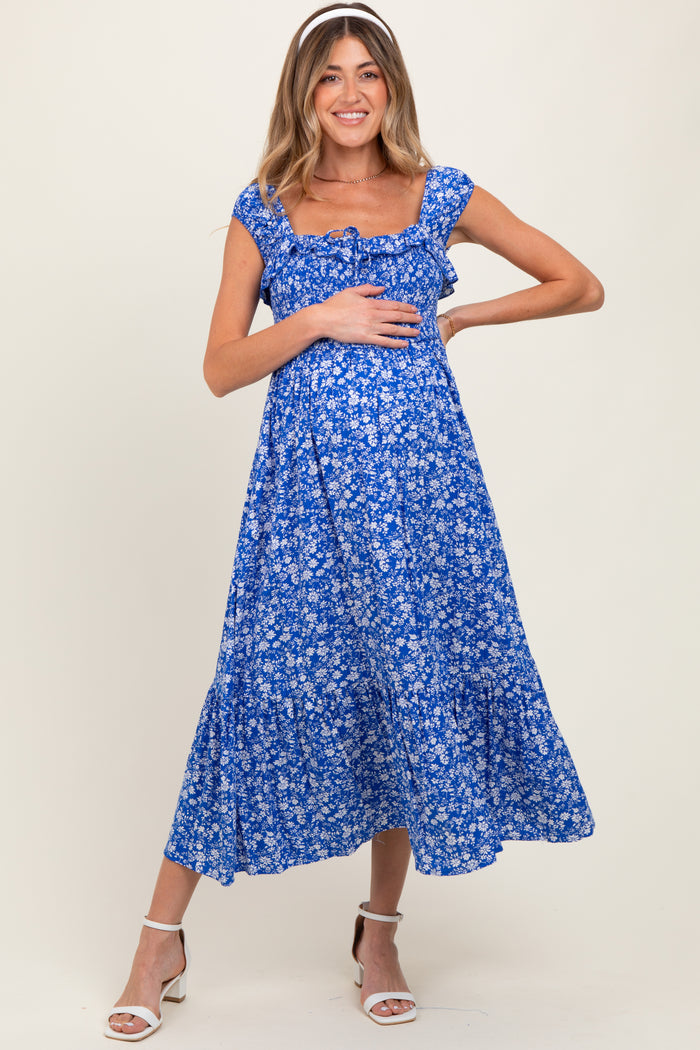 woman wearing a blue floral maternity dress with ruffle sleeves and holding her baby bump