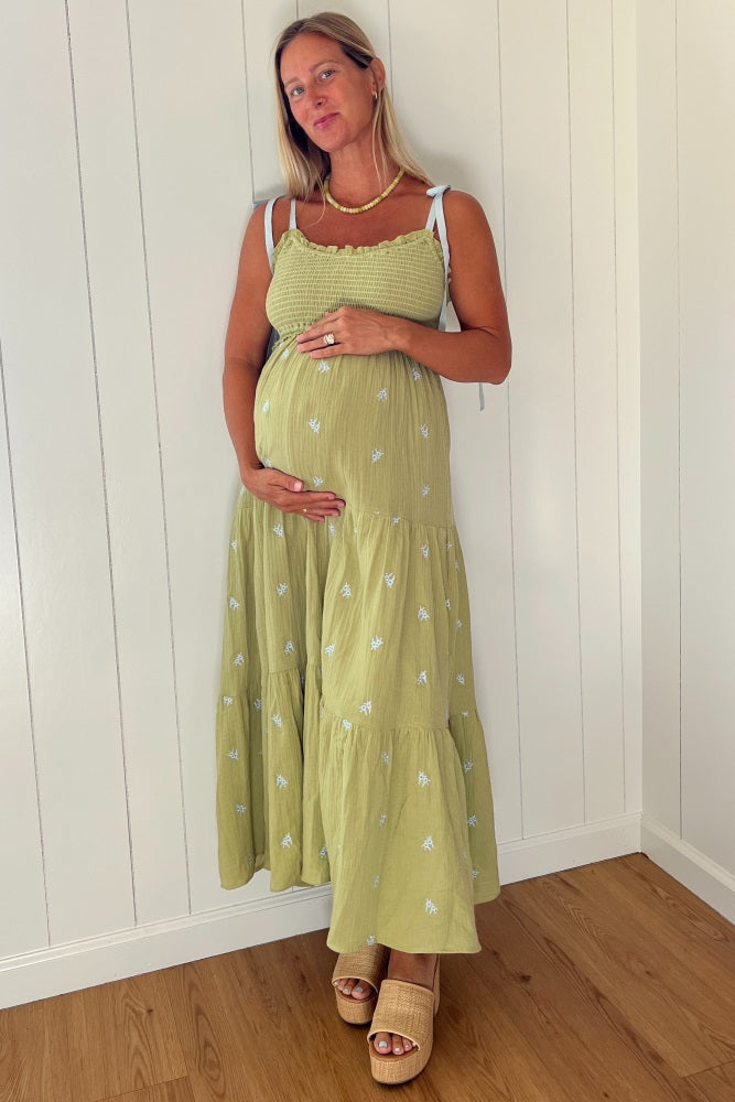 woman wearing a light green maternity maxi dress with a ruched bodice and tiered skirt, cradling her baby bump