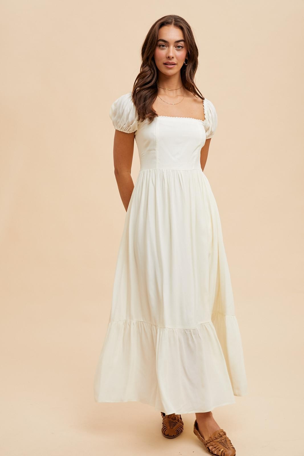 woman wearing a long white puff sleeve dress with a square neckline and tiered bottom