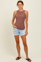 woman wearing a brown ribbed tank top and distressed light blue denim shorts, standing with one hand in her pocket