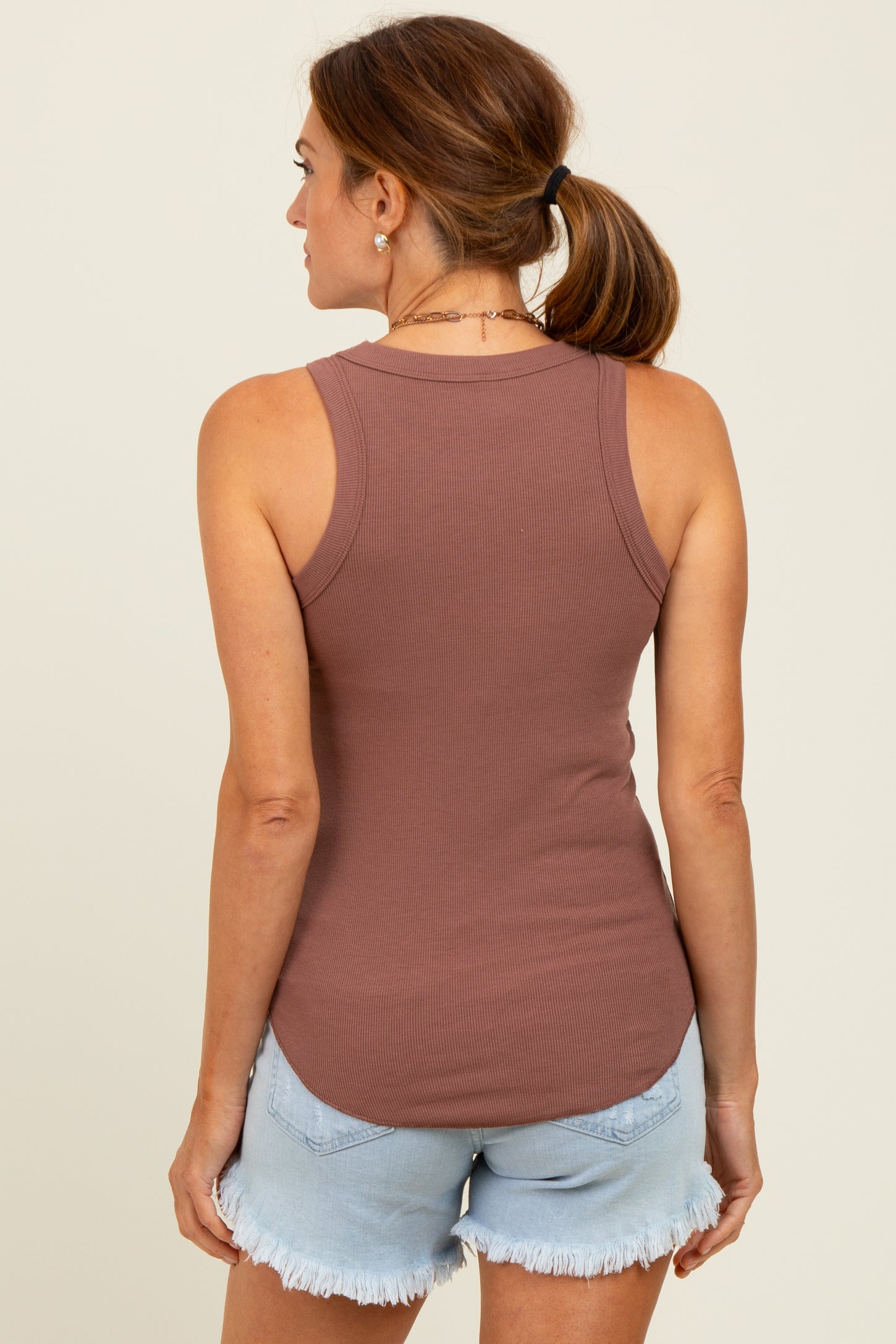 woman wearing a brown ribbed tank top and light denim shorts, seen from the back