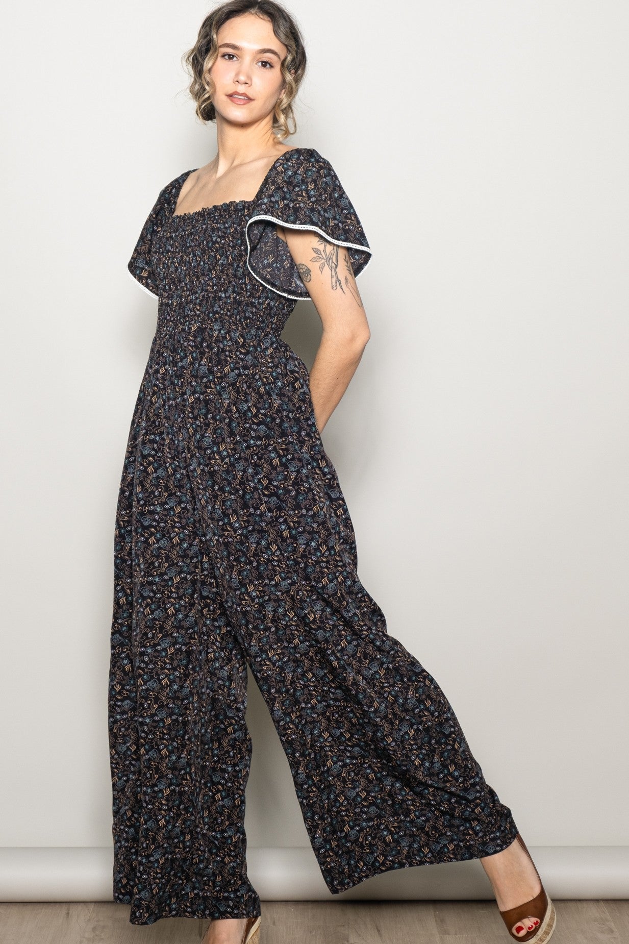 woman wearing a navy blue floral smocked jumpsuit with flutter sleeves and wide-leg pants