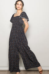 woman wearing a navy blue floral smocked jumpsuit with flutter sleeves and wide-leg pants