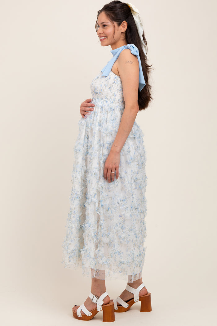 woman wearing a light blue floral maternity dress with a bow detail, showing her baby bump and posing sideways