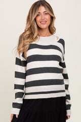 woman wearing a striped black and cream maternity sweater with cutout details and a visible baby bump