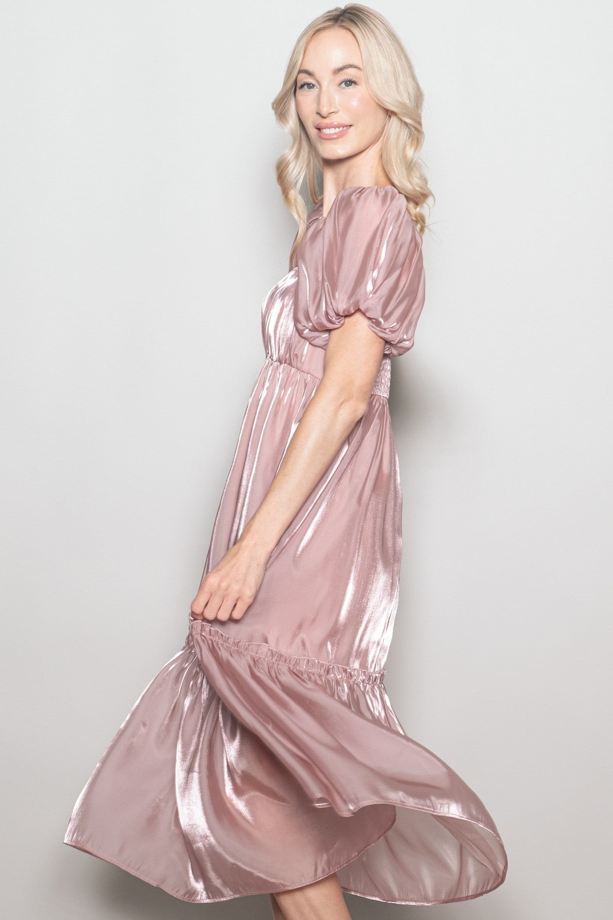 woman wearing a rose gold satin puff sleeve midi dress with a flowy skirt, smiling and posing sideways