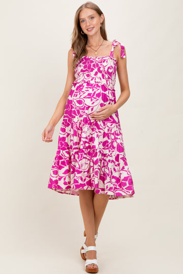 woman wearing a pink floral maternity dress with tie straps and a visible baby bump