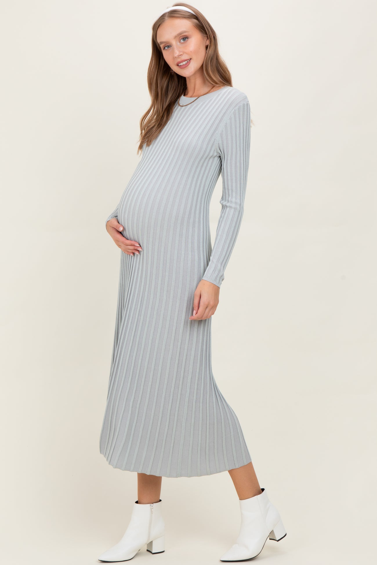 woman wearing a light grey ribbed maternity dress, holding her baby bump, and wearing white ankle boots