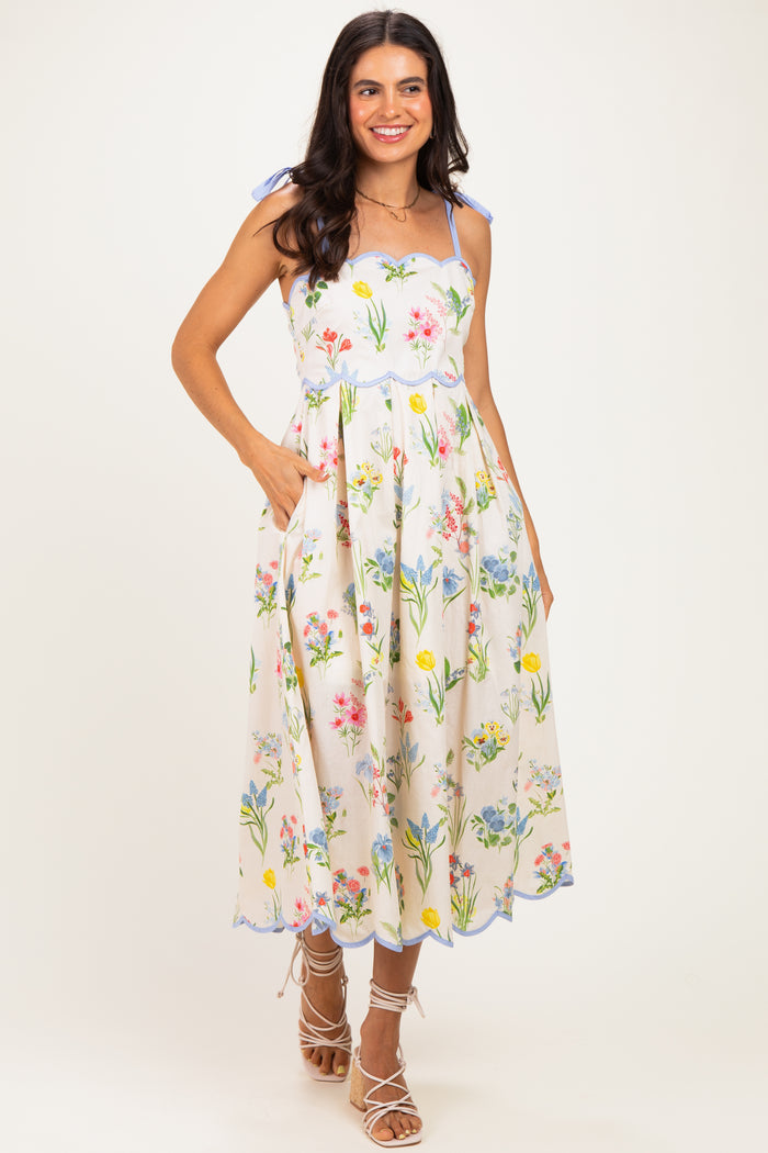 woman wearing a floral midi dress with spaghetti straps and pockets, featuring colorful flowers on a cream background