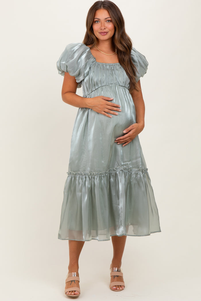 woman wearing a pale green satin maternity dress with puff sleeves and a tiered skirt, displaying her baby bump