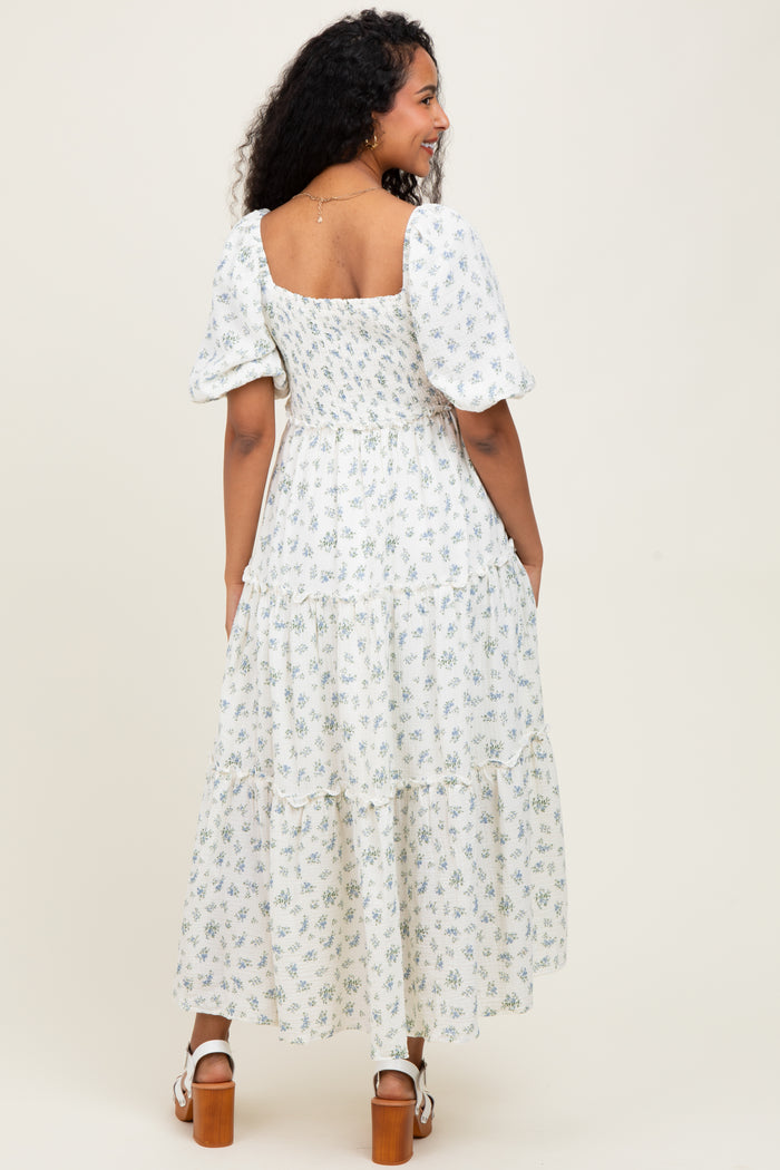 woman wearing a white floral print maternity maxi dress with puff sleeves and a tiered skirt