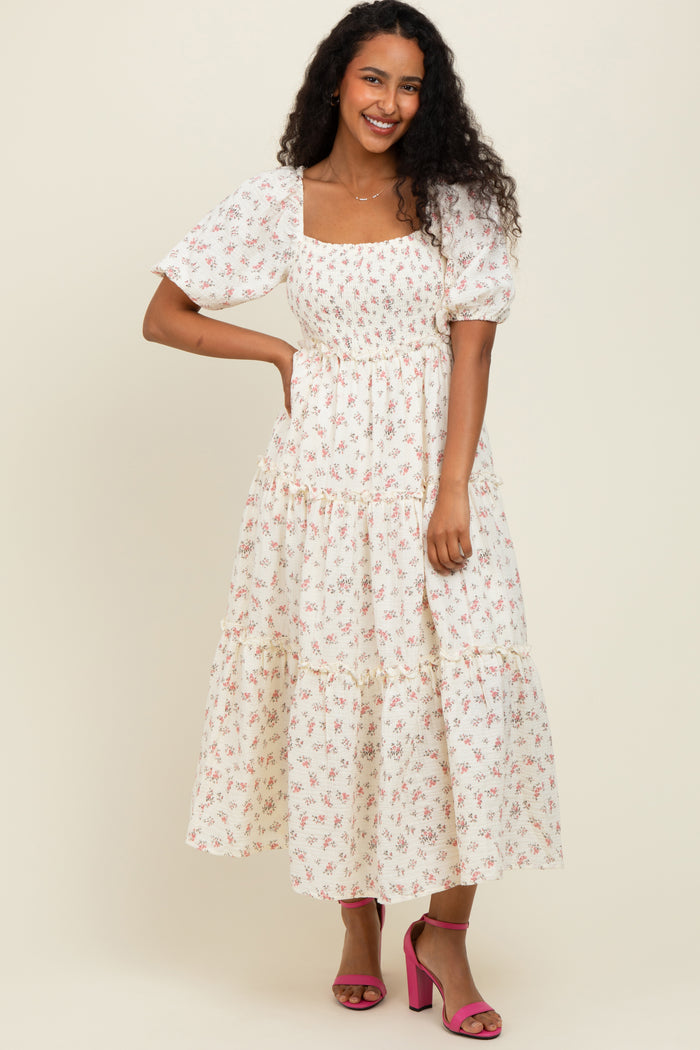 woman wearing a white puff sleeve floral maxi dress and pink heels, smiling against a neutral background