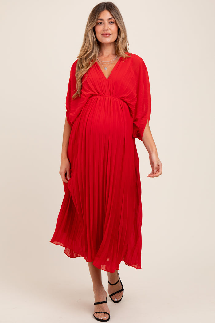 woman wearing a flowing red maternity dress with pleated skirt and v-neckline, showcasing her baby bump