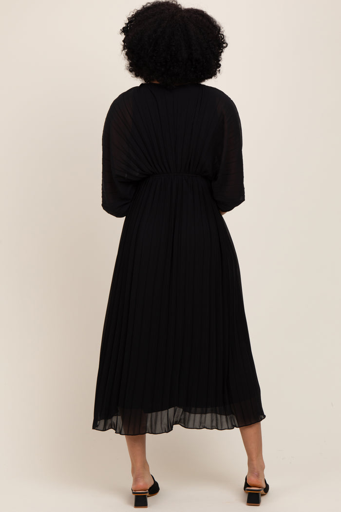 woman wearing a black pleated midi dress with a flowy silhouette and short sleeves, seen from the back