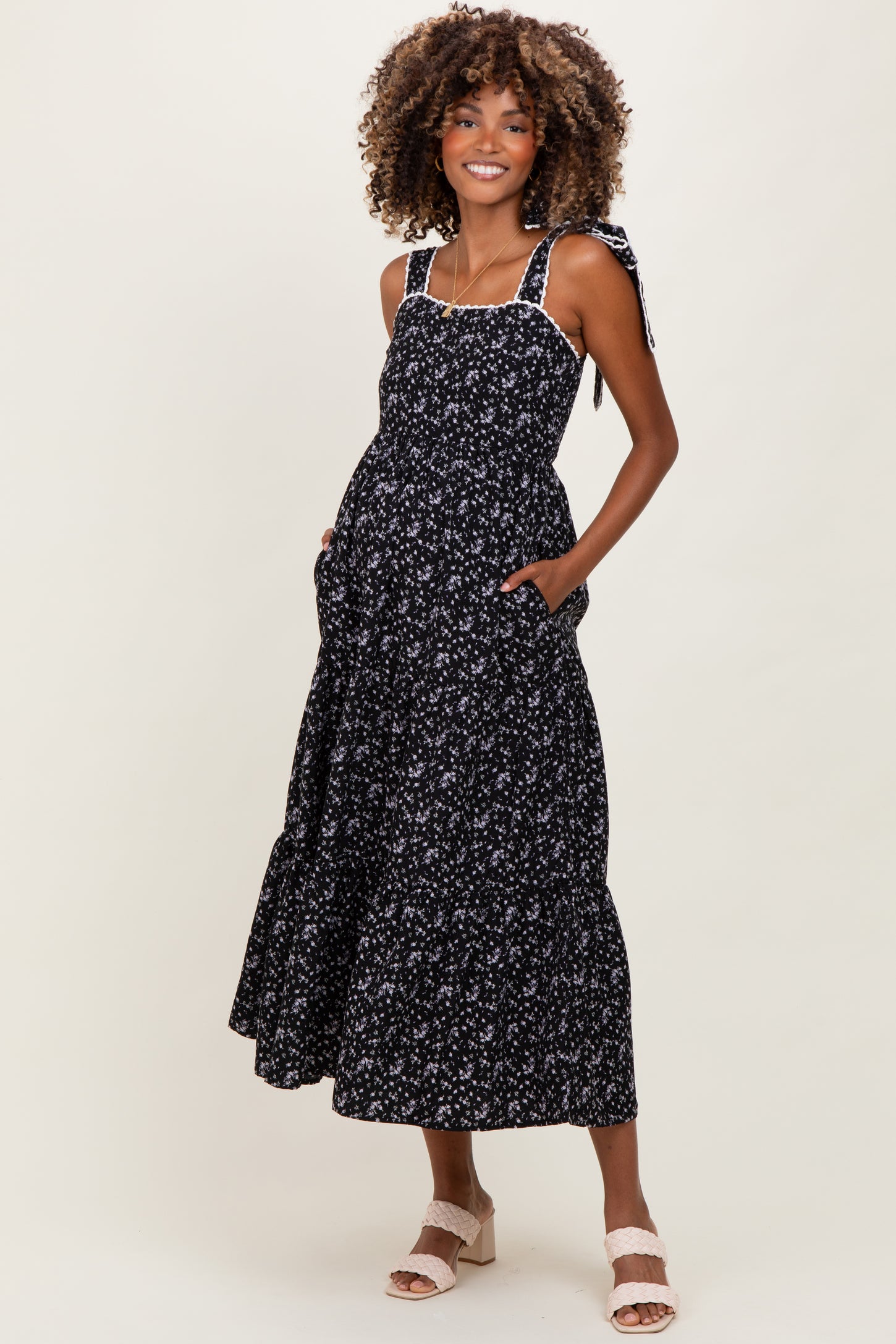 woman wearing a black floral maternity maxi dress with tie shoulder straps and pockets, showing baby bump