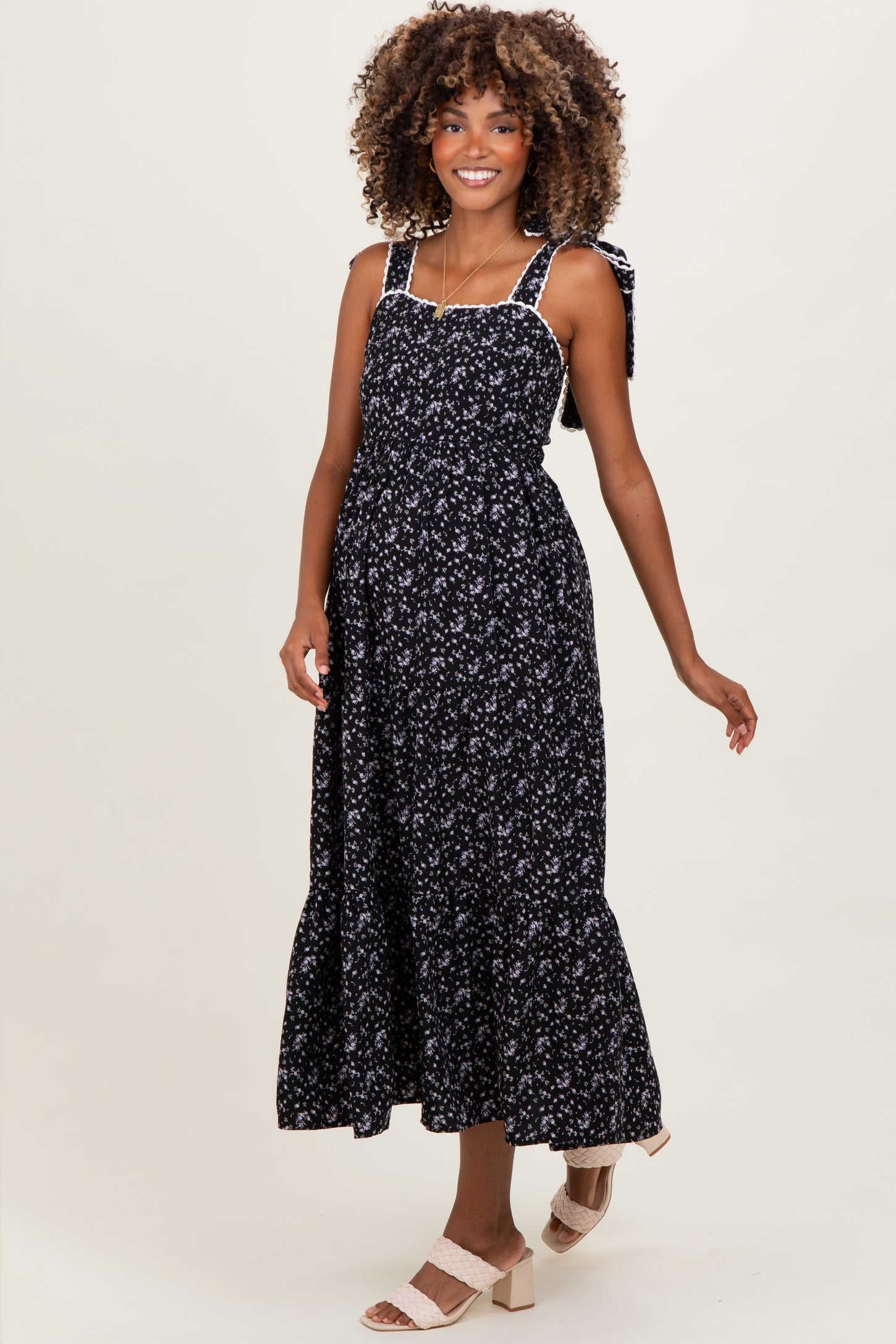 woman wearing a black floral maternity maxi dress with tie straps and a flowing skirt, showing her baby bump