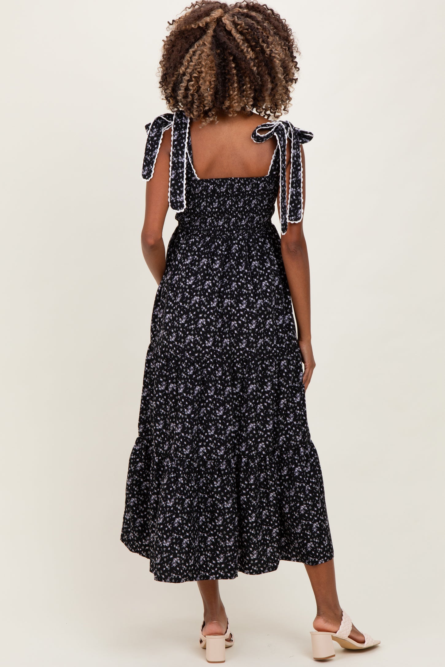 woman wearing a black floral maternity dress with tie straps and a tiered skirt, seen from the back