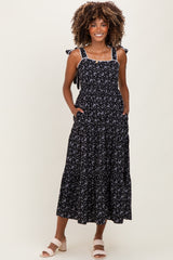 woman wearing a black floral print maternity dress with tie straps and pockets, showcasing a baby bump
