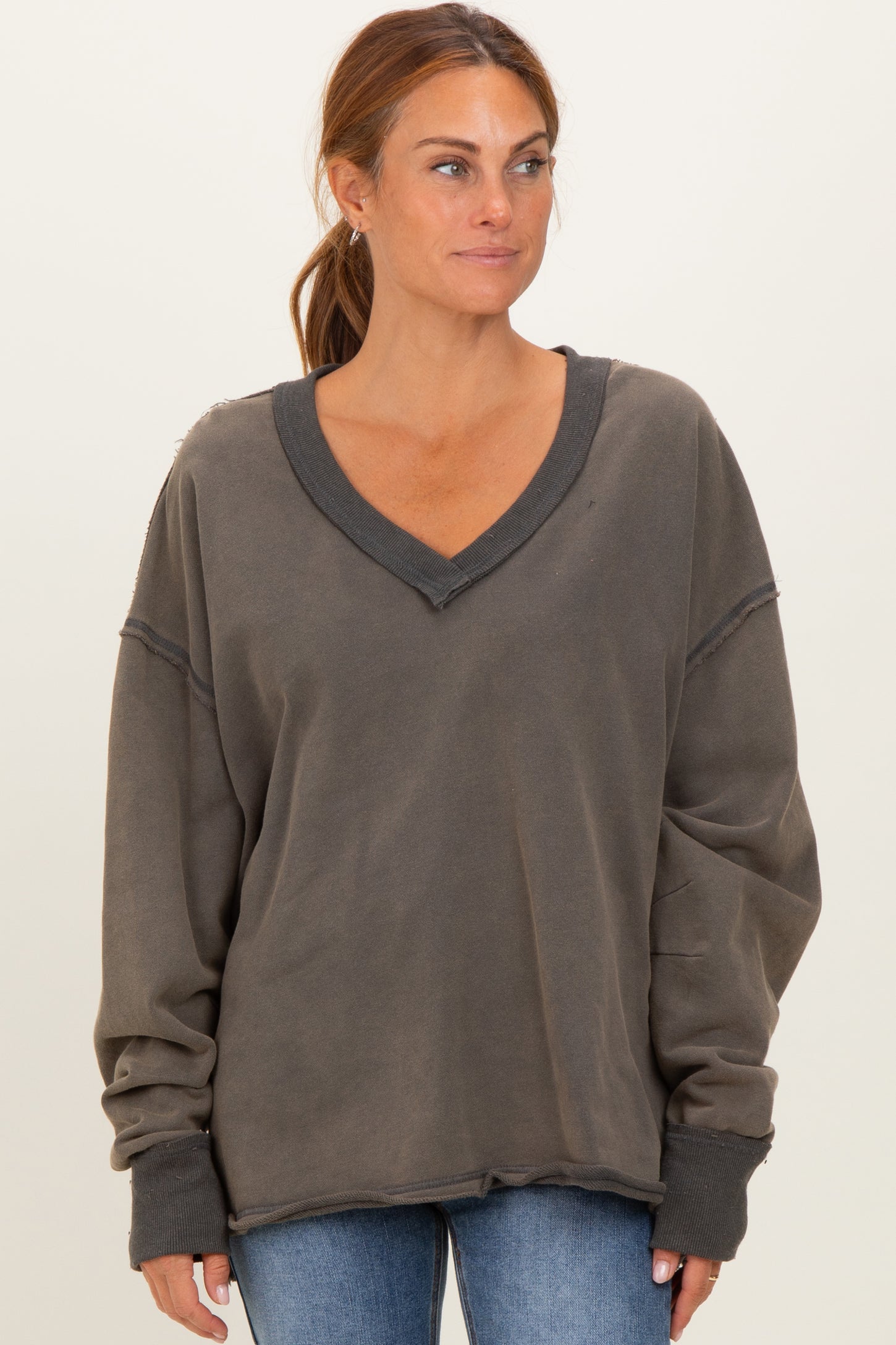woman wearing a dark gray oversized v-neck sweatshirt with raw hem and long sleeves